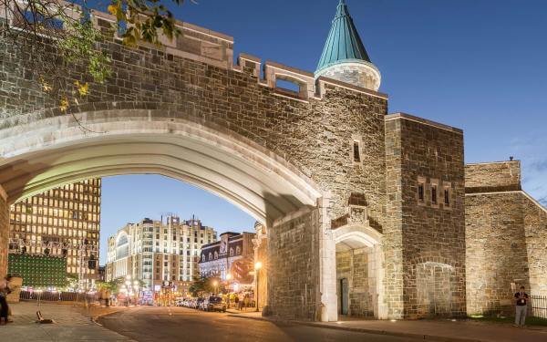 Saint-Jean Gate illuminated in the early evening, with the Hotel Palace Royal in the background.