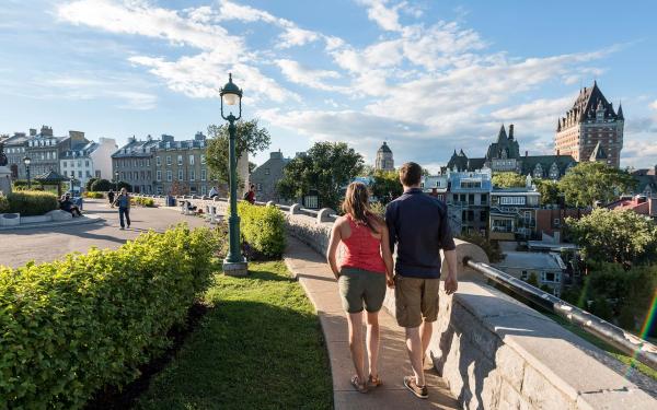 A couple walk on the Pierre-Dugua-De Mons terrace near Avenue Saint-Denis, looking at the Château Frontenac.