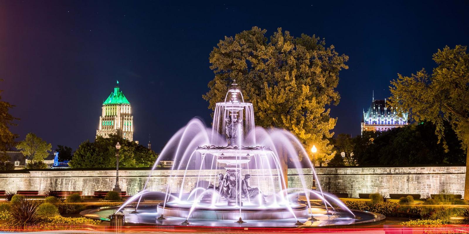 Fontaine de Tourny la nuit avec le Château Frontenac et l'édifice Price illuminés à l'arrière-plan.