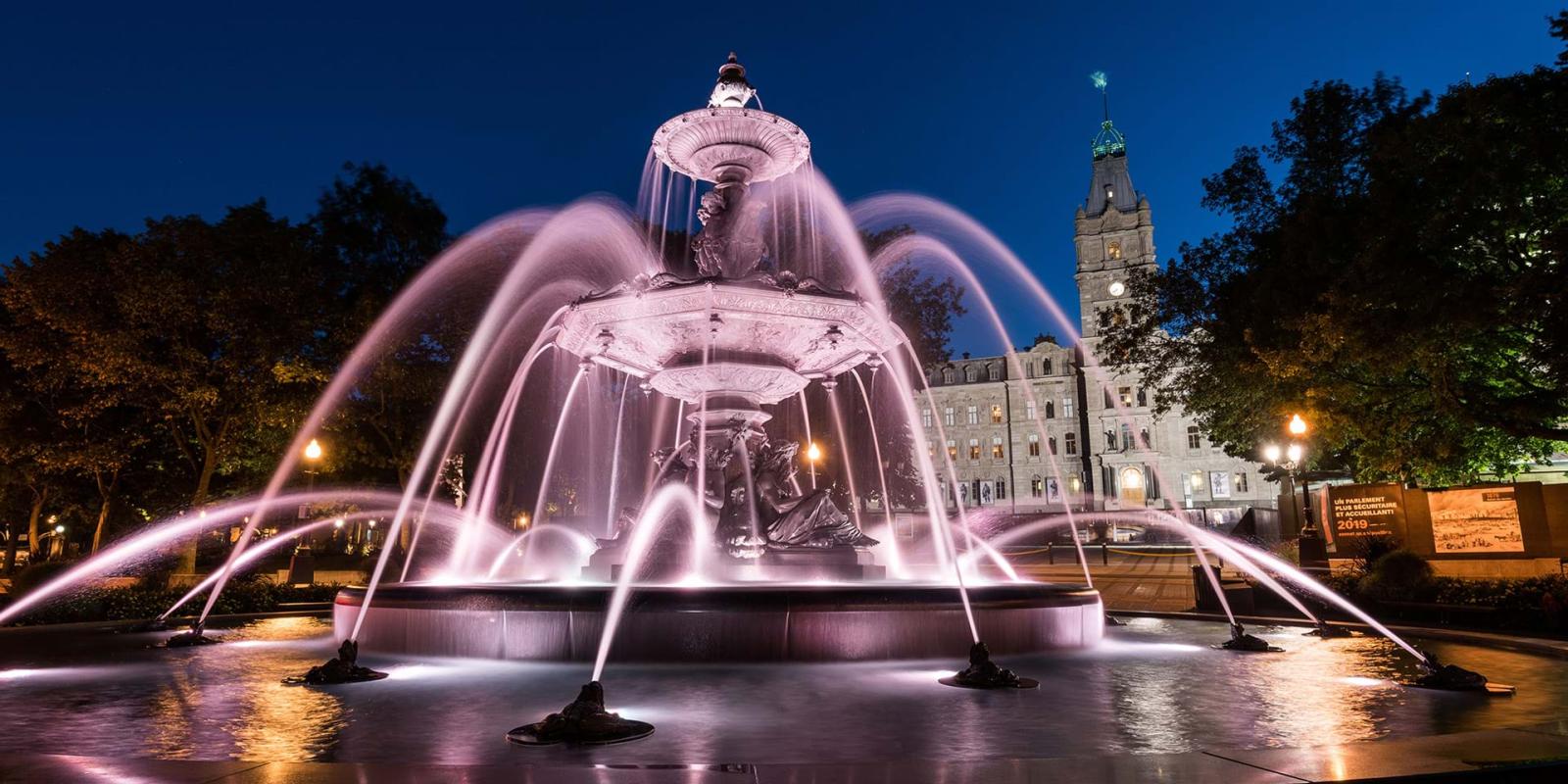 Vue de la Fontaine de Tourny illuminée en soirée et l'Hôtel du Parlement en arrière-plan.