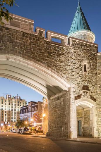 Saint-Jean Gate illuminated in the early evening, with the Hotel Palace Royal in the background.