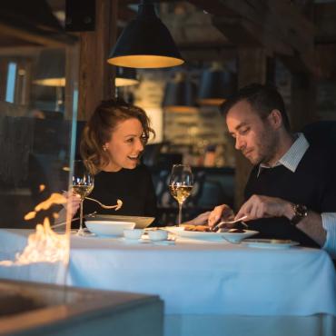 A couple enjoy a gourmet meal at Chez Muffy restaurant, in front of a fireplace.
