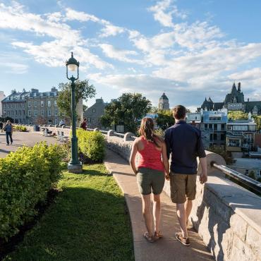 A couple walk on the Pierre-Dugua-De Mons terrace near Avenue Saint-Denis, looking at the Château Frontenac.